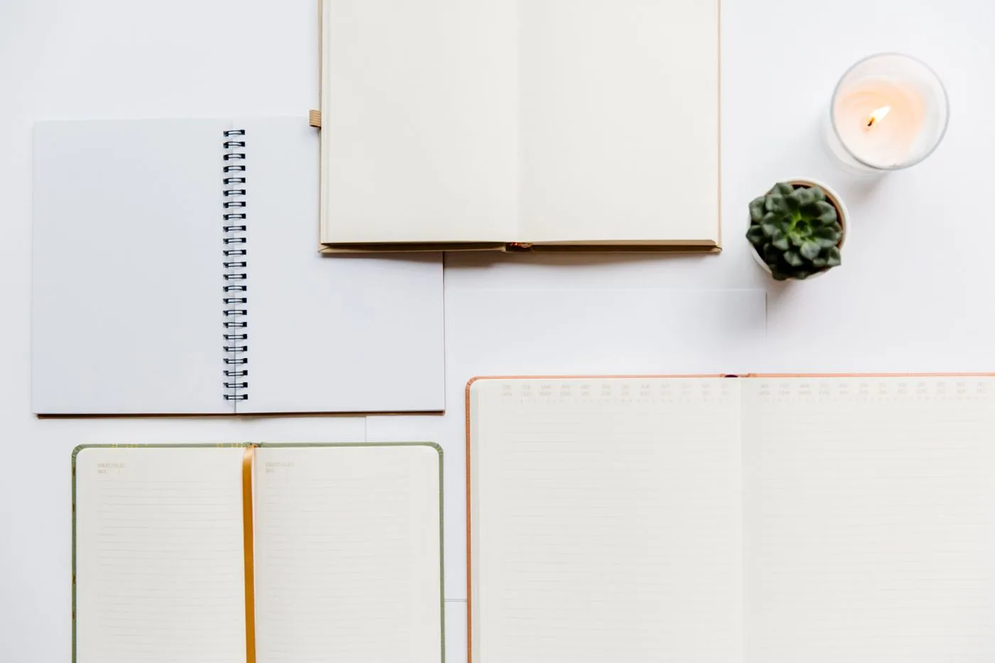 An open journal on a desk beside a lit candle and a small potted plant