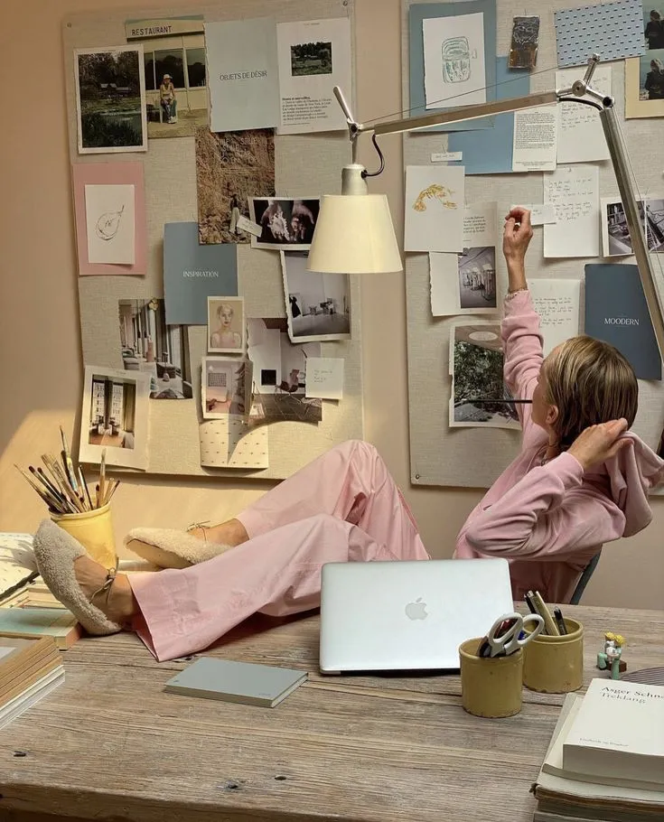 A woman relaxing at her desk beside a vision board and laptop