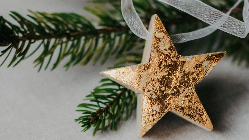 A gold star ornament on a pine twig beside a dark green velvet ribbon