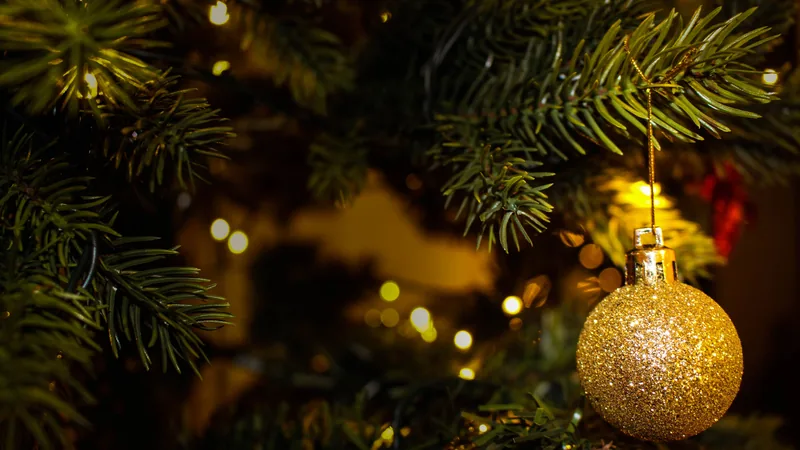 A gold bauble hanging in a lit Christmas tree