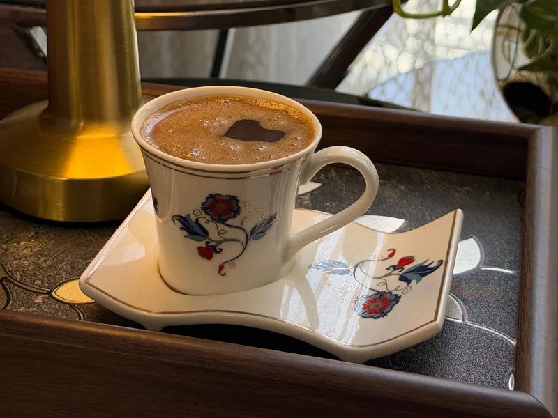 A cup of coffee on a decorated tray beside a brass lamp in soft evening light