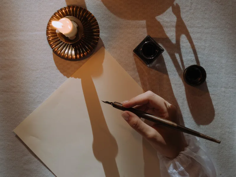 A hand holding a quill pen over a blank sheet of paper