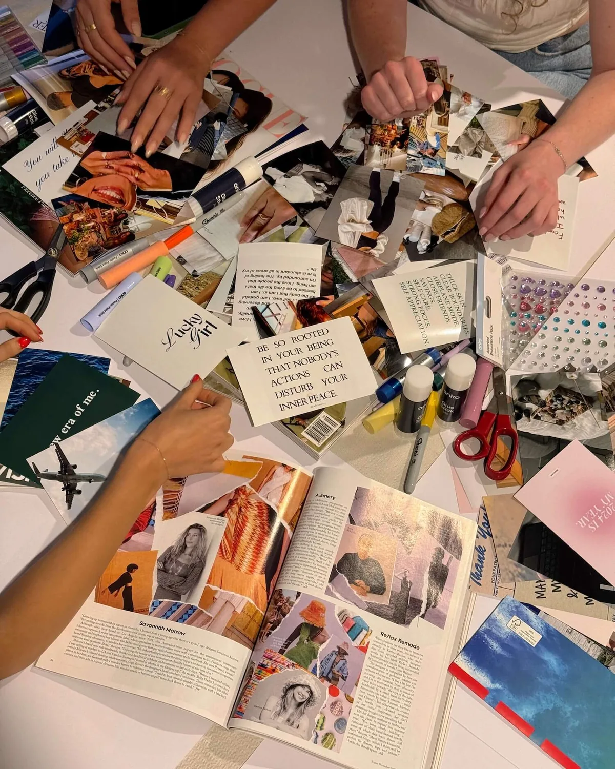 Several hands cutting pictures out of magazines on a crowded table for their vision boards