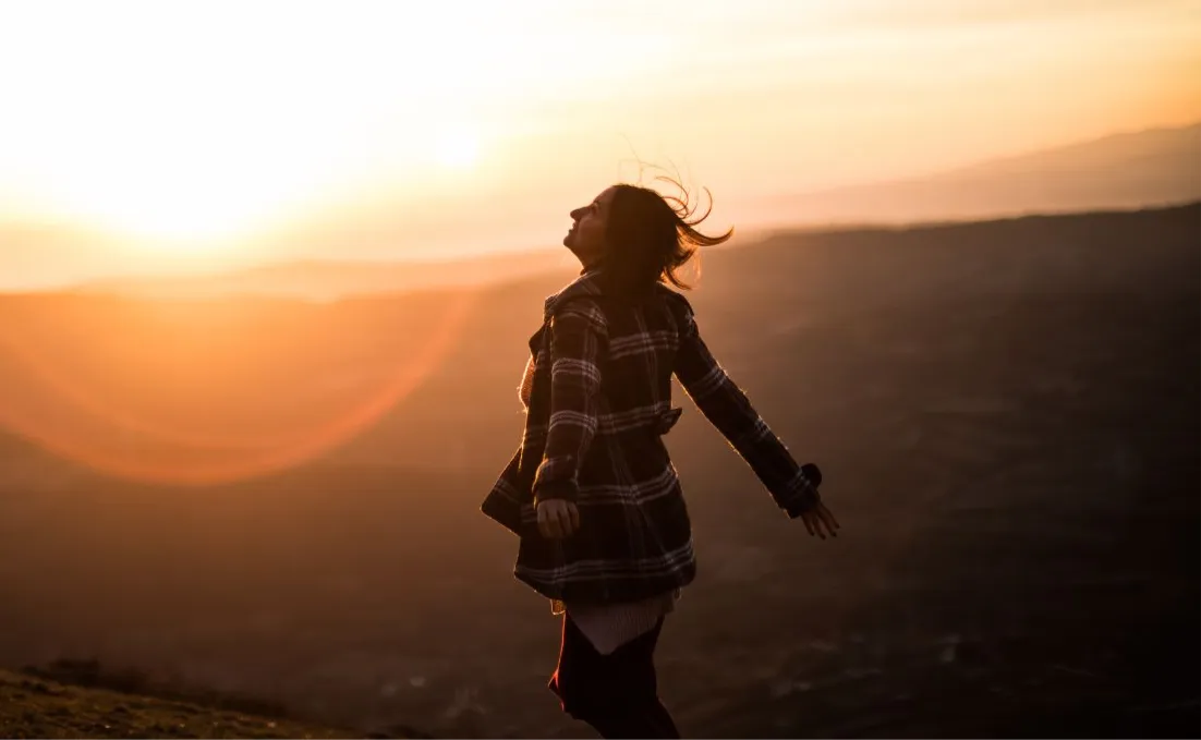 Eine Frau auf einem Hügel bei Sonnenaufgang, die Arme geöffnet, im goldenen Licht