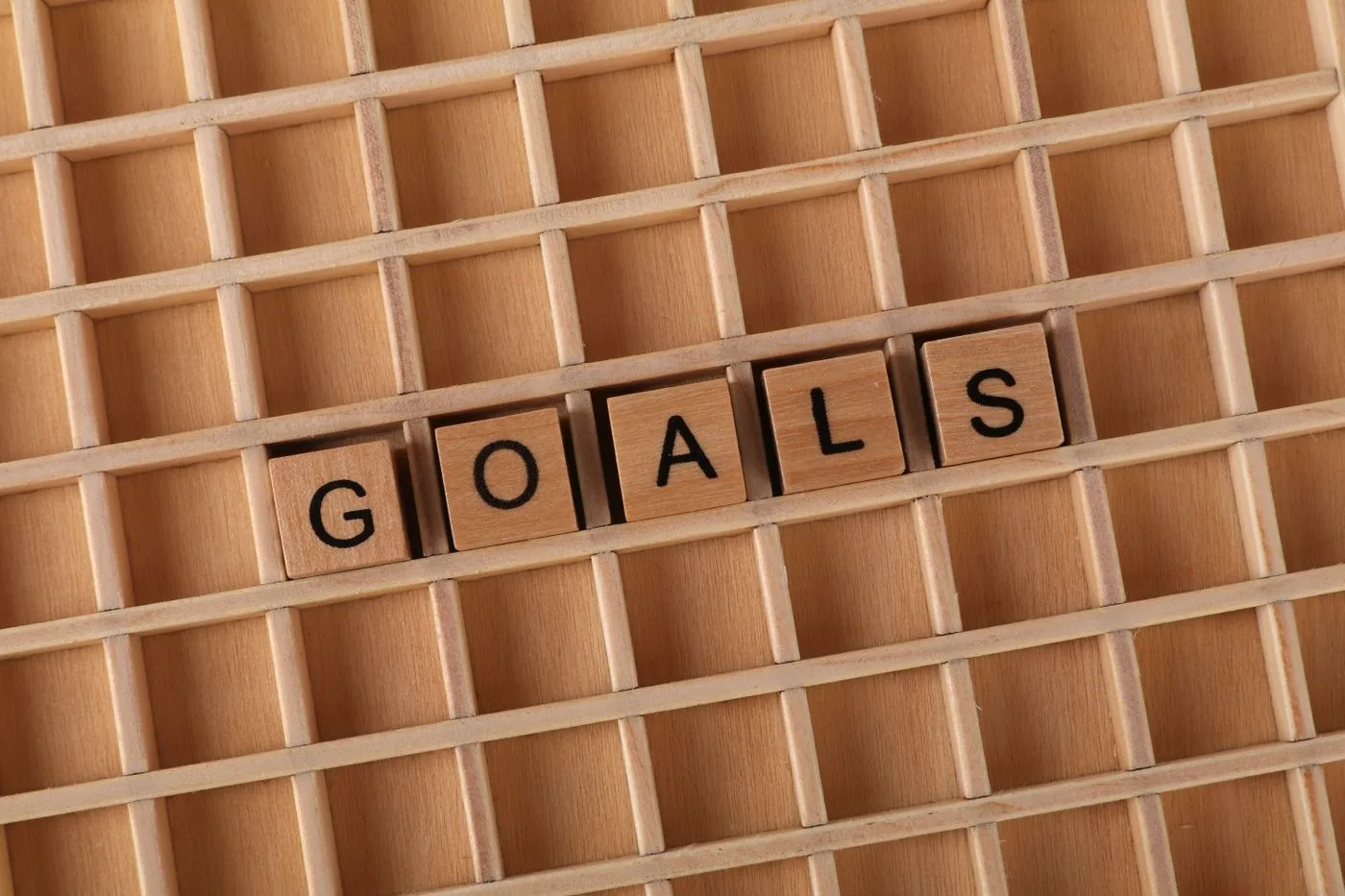 Wooden letter blocks spelling the word “Goals” arranged on a wooden grid