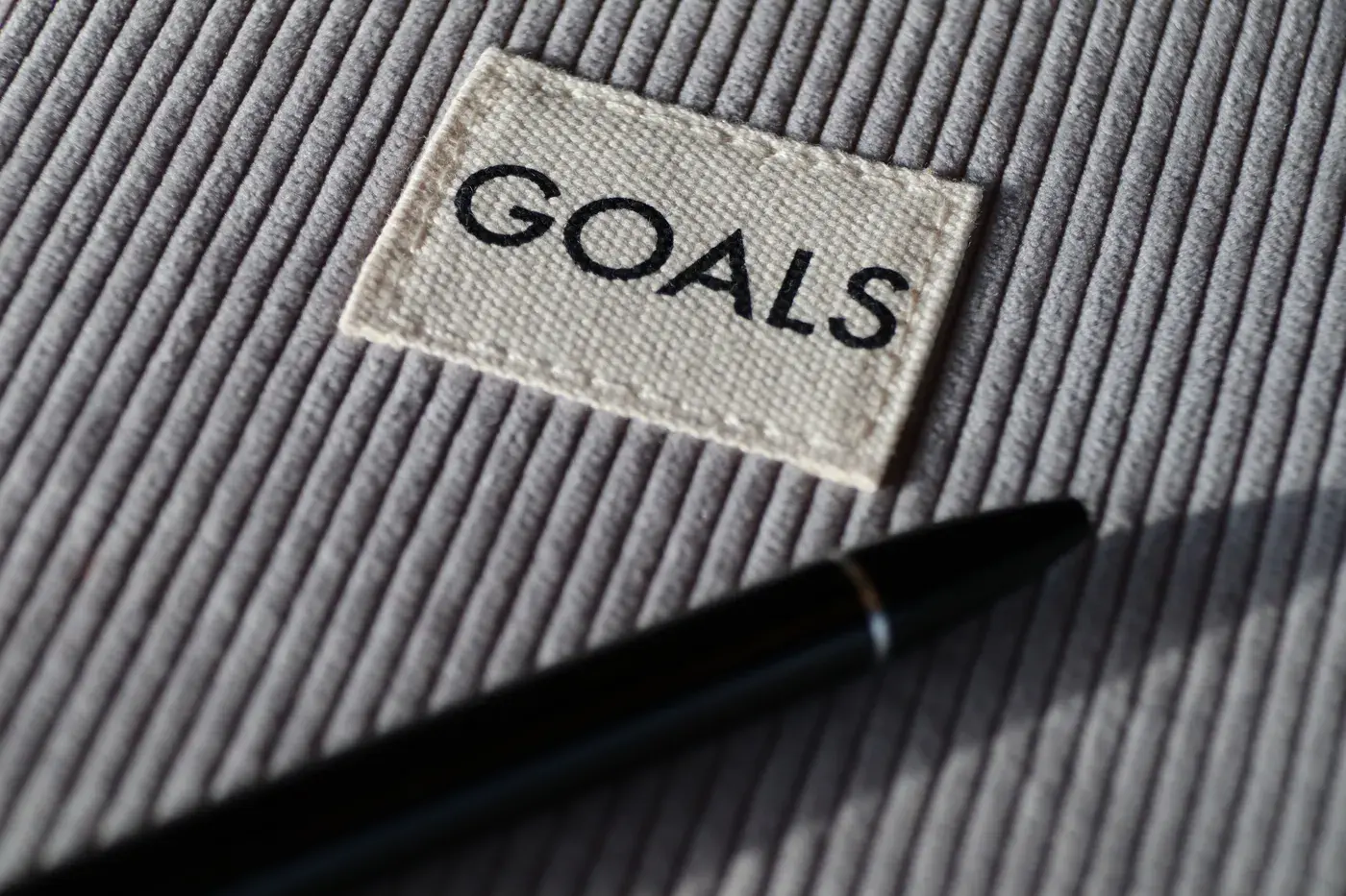 Тканевая нашивка с надписью «GOALS» на сером рубчатом полотне, рядом лежит чёрная ручка