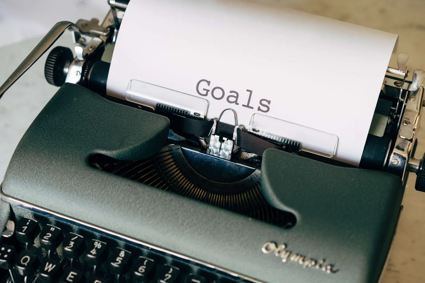 A vintage green Olympia typewriter with a sheet of paper reading the single word 'Goals'