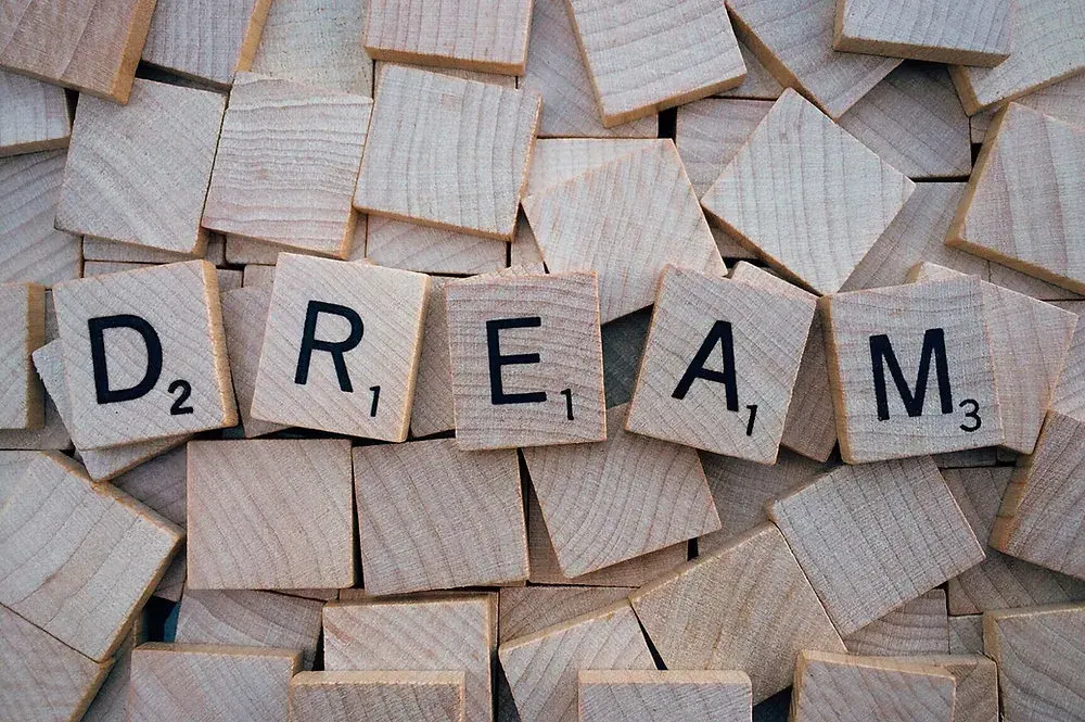 Деревянные плитки с буквами, выложенные в слово DREAM, среди россыпи фишек
