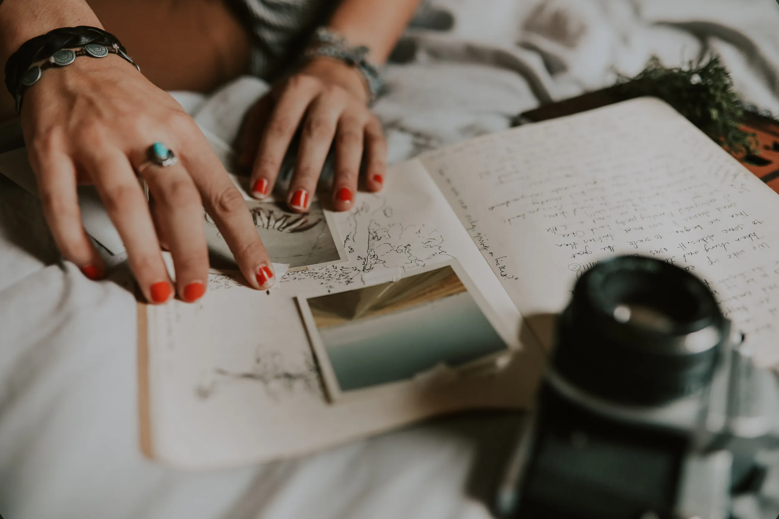 Hände mit rotem Nagellack ordnen Fotos in ein aufgeschlagenes Reisetagebuch, daneben eine analoge Kamera
