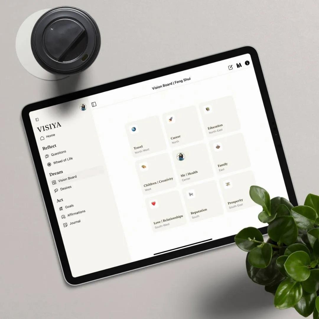 VISIYA app on a tablet showing a Feng Shui vision board in Bagua sectors, beside coffee and a plant