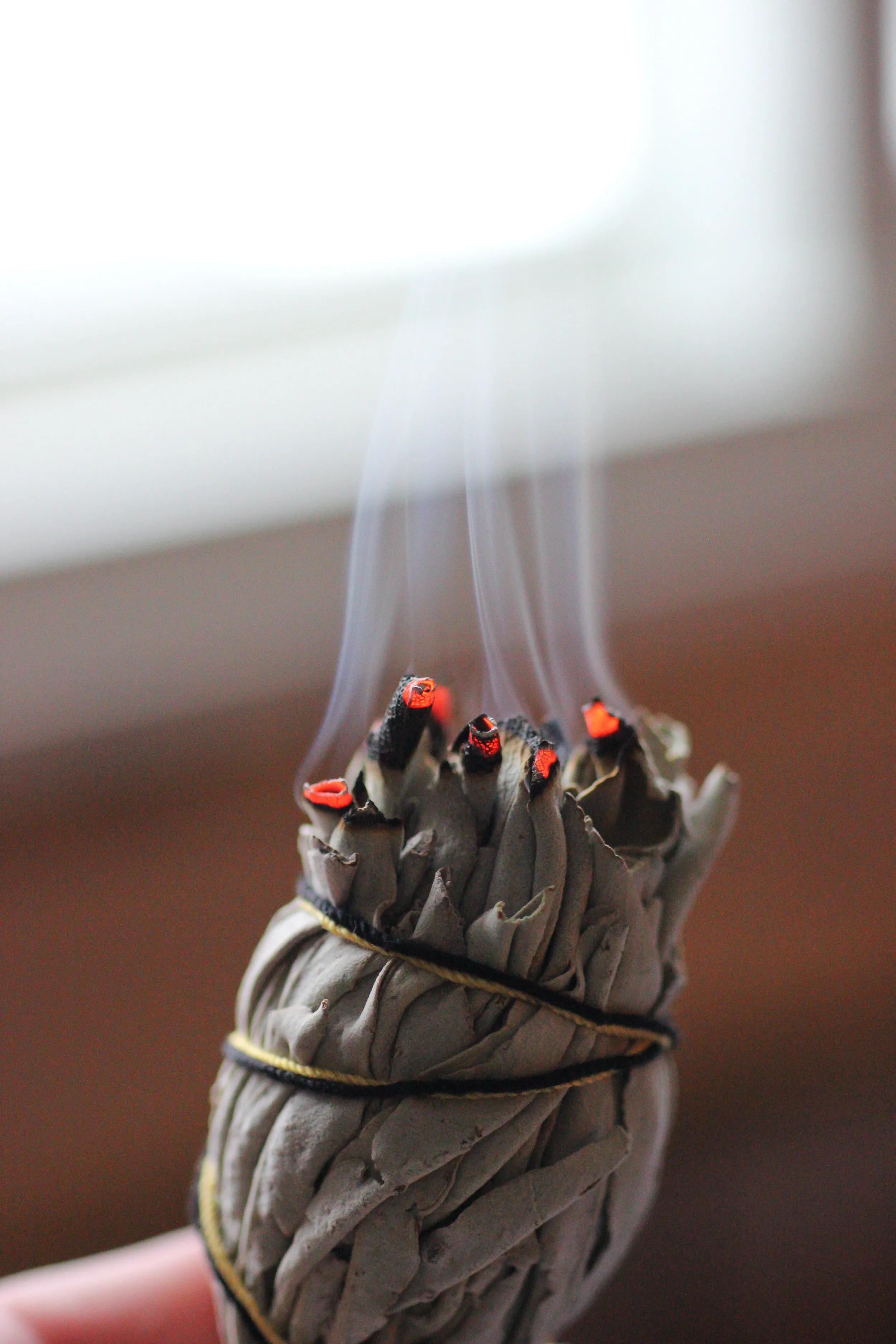Bound white sage smudge stick glowing with embers, smoke curling upward for a sacred new-year cleansing ritual