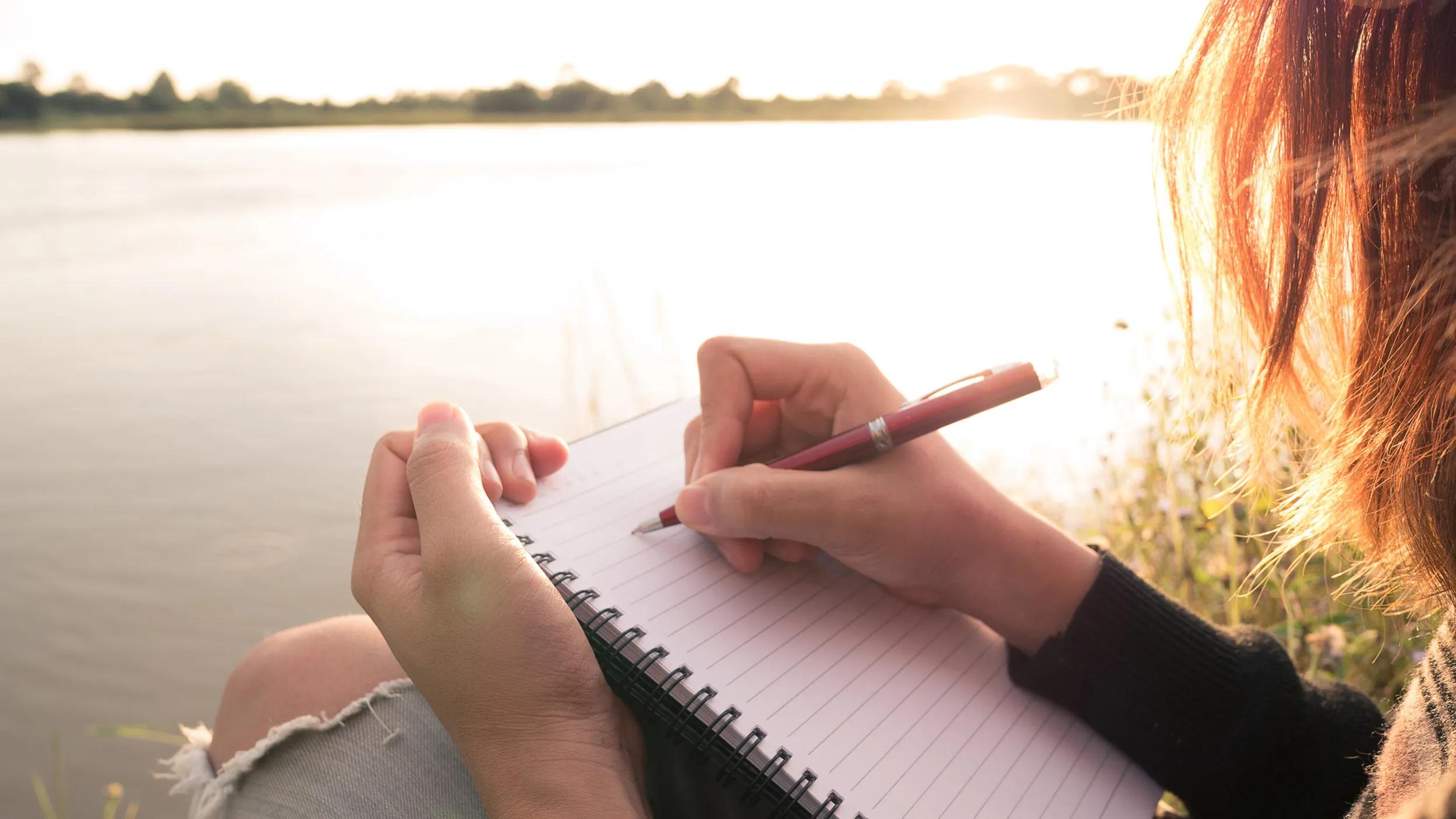 Eine junge Frau schreibt in der Abenddämmerung am Fluss in ihr Tagebuch – die Methode von Dr. Ira Progoff