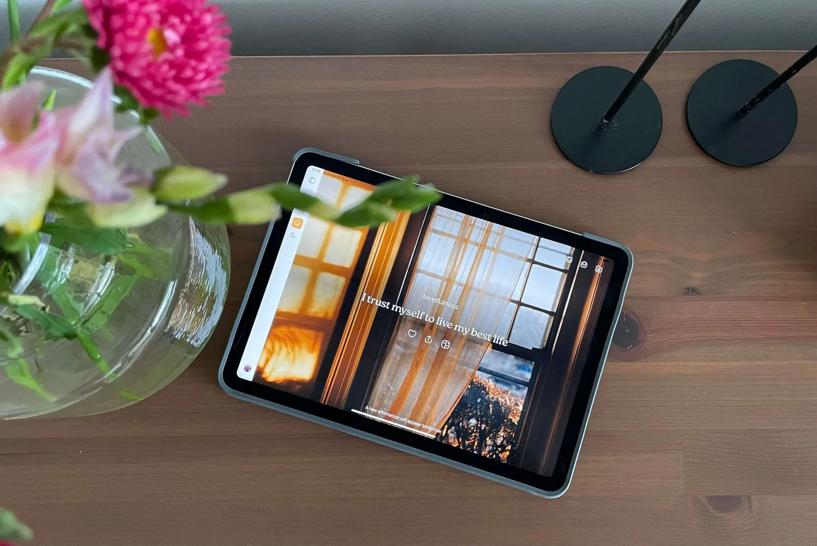 iPad лежит на полу с аффирмацией VISIYA «I trust myself to live my best life», рядом стеклянная ваза с розовыми цветами