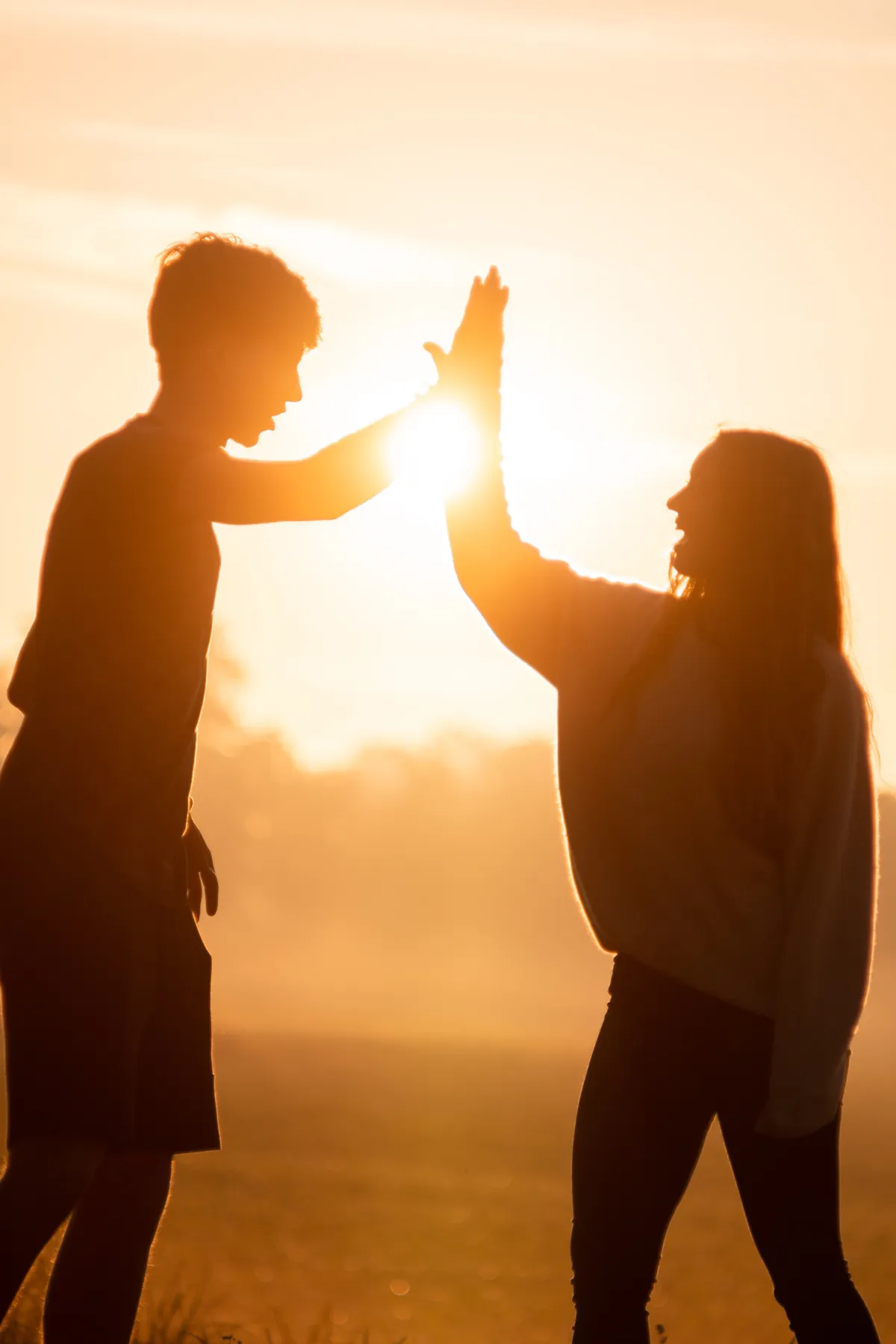 Zwei Freunde klatschen sich als Silhouetten vor einem warmen goldenen Sonnenuntergang ab